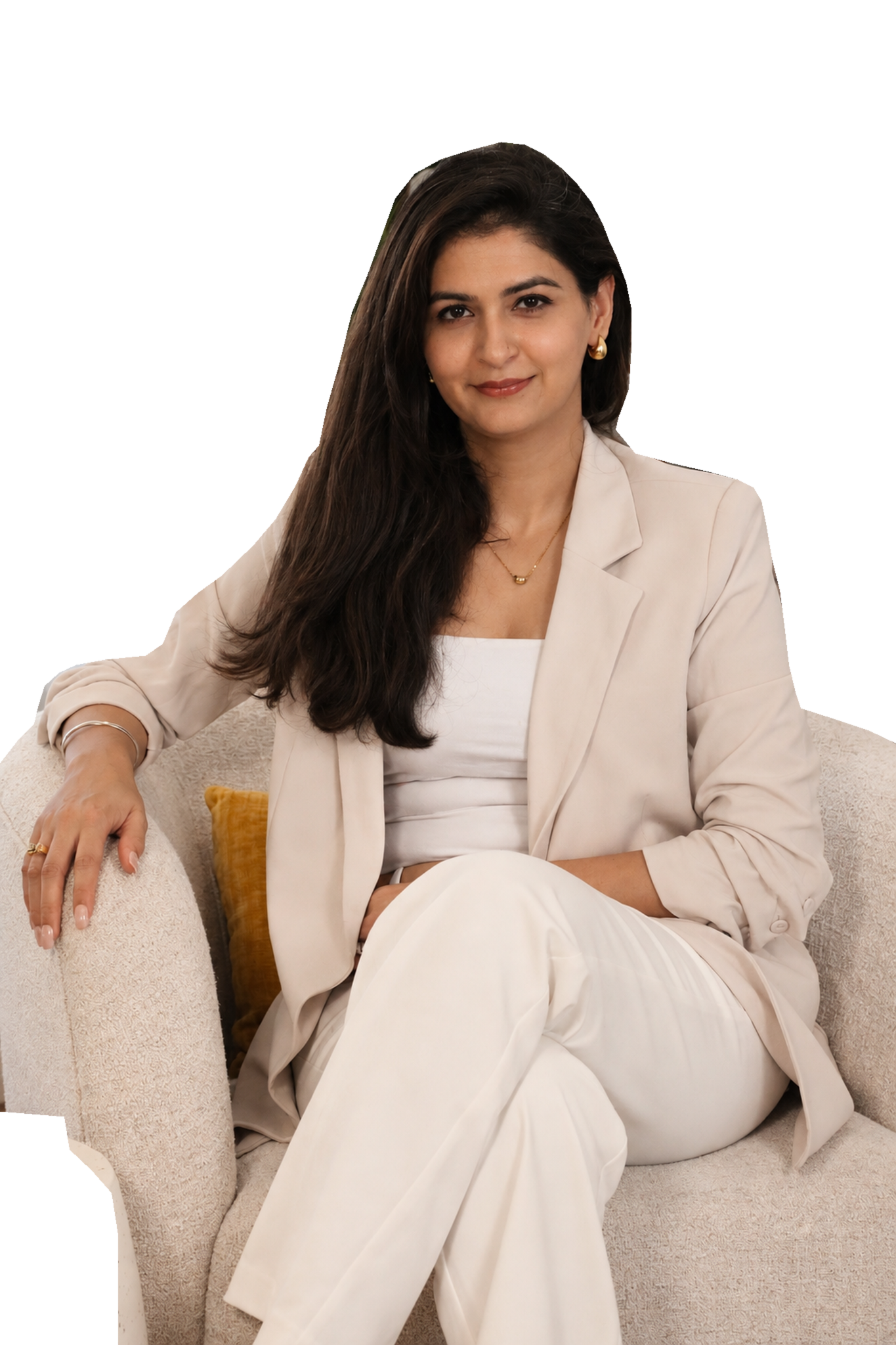 Ravneet Kaur seated in her cream chair, wearing her ivory suit and looking at the camera.