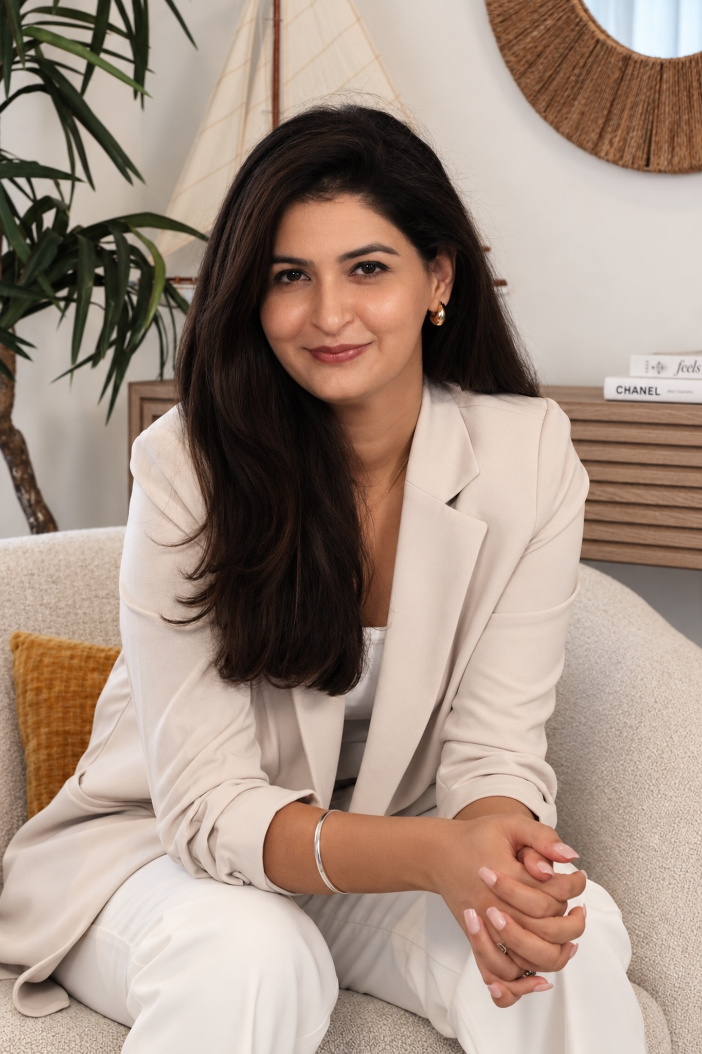 Ravneet seated confidently on a sofa, wearing her ivory suit and looking at the camera.